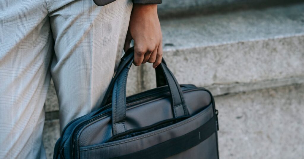 Crop anonymous person in stylish outfit carrying laptop in bag while walking along street