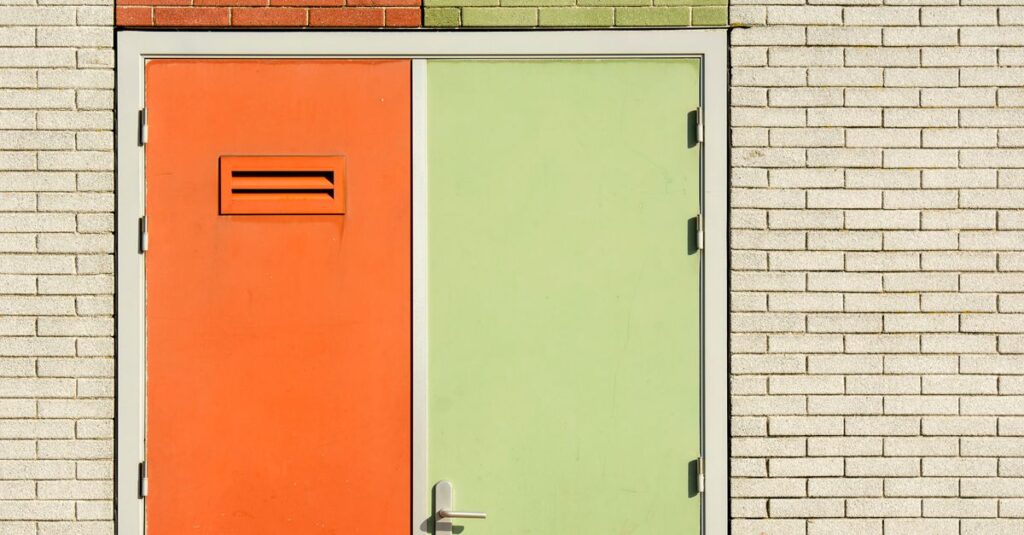 Orange and green door on a brick wall with modern design and security features.