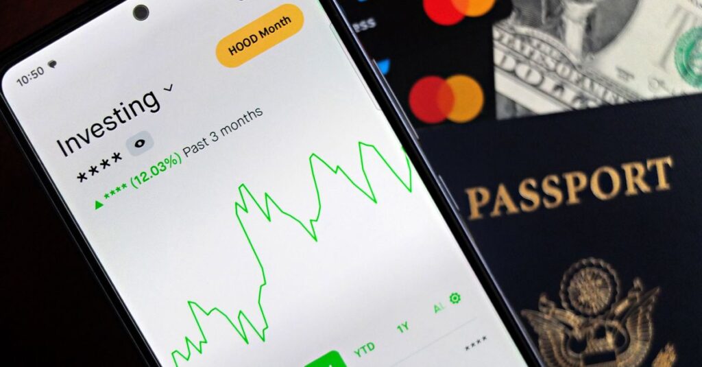 Smartphone showing stock market app with travel essentials: passport, money, and cards.