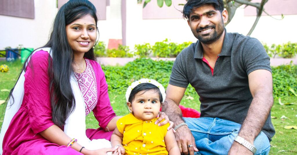 A happy family with parents and a toddler enjoying quality time sitting on a grassy lawn outdoors.
