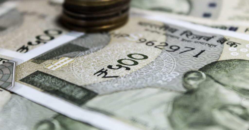 Detailed image of Indian Rupees banknotes with a stack of coins, emphasizing currency details.